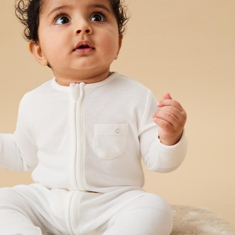 A baby in a white zip sleepsuit