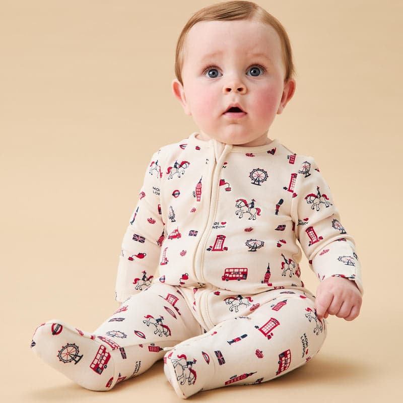A baby in a cream London-print sleepsuit