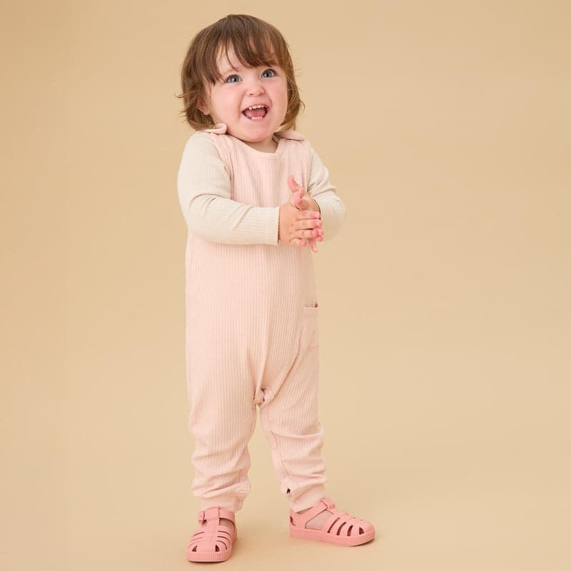 A baby in blush ribbed dungarees