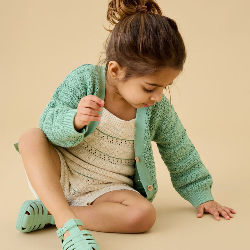 A child in a cream knitted romper and sage cardigan