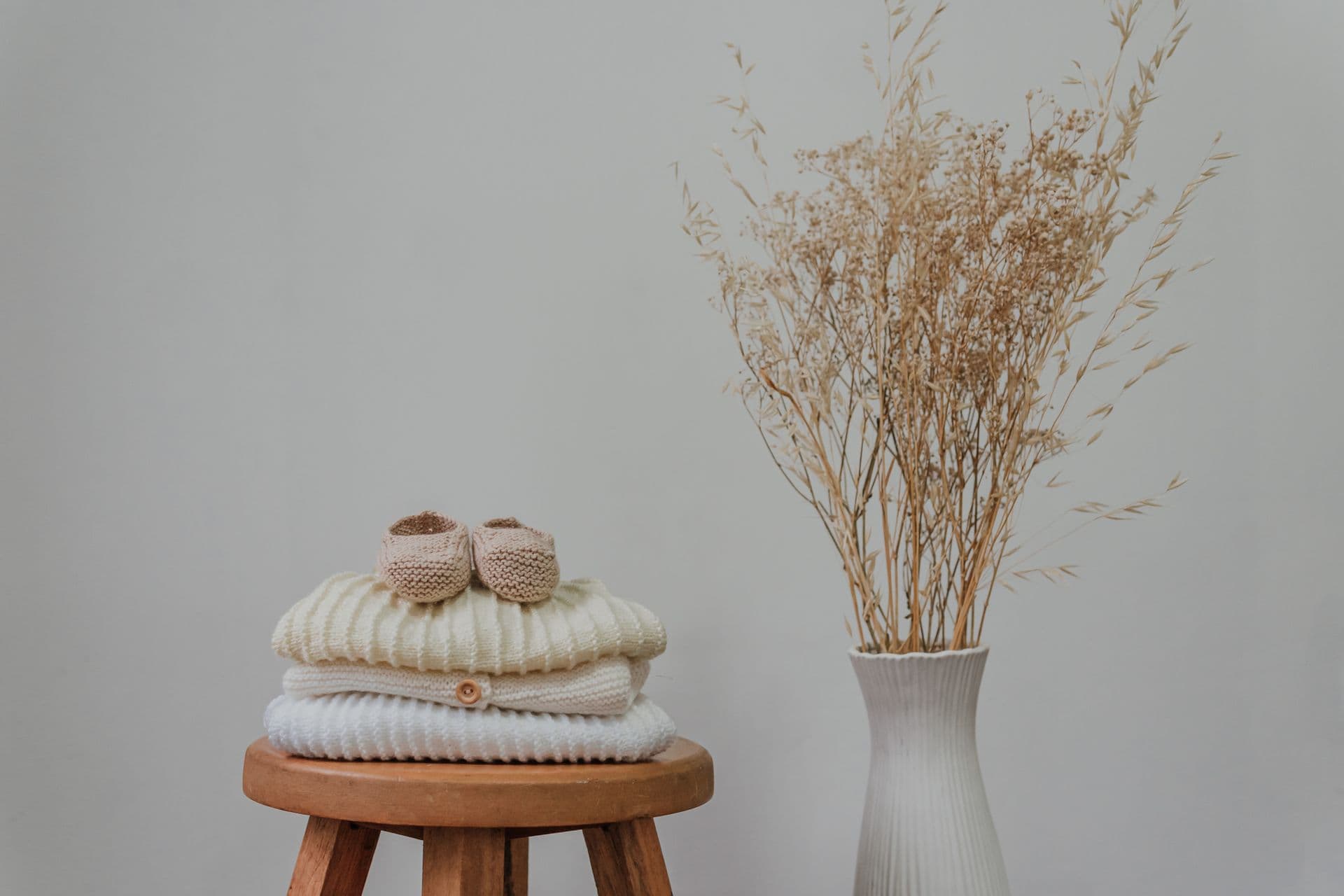 A soft stack of cream knitted baby clothes and booties on a wooden stool