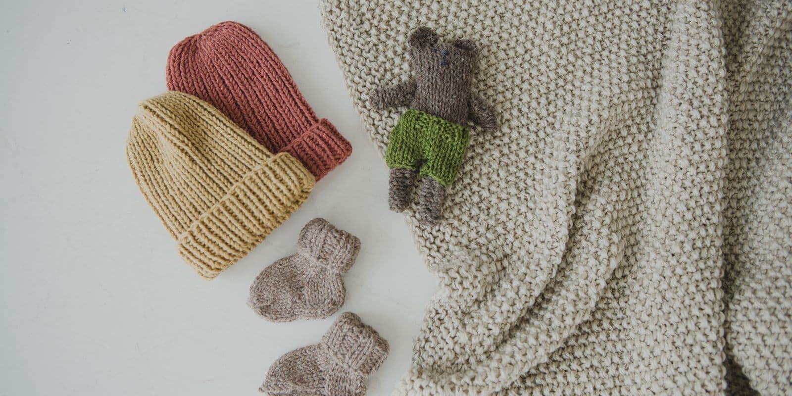 A flat-lay of knitted baby hats, booties and blankets