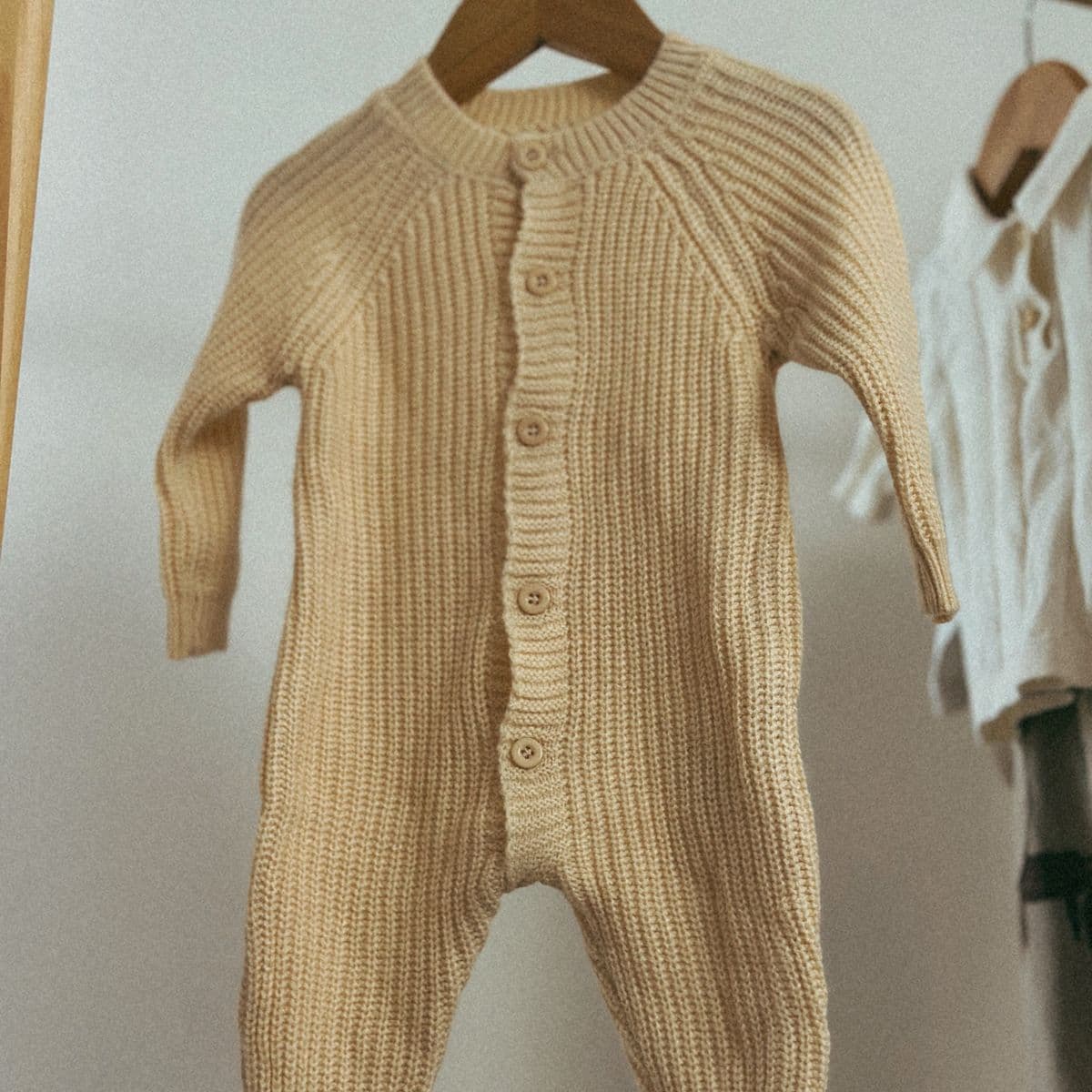 A beige ribbed-knit baby romper on a wooden hanger