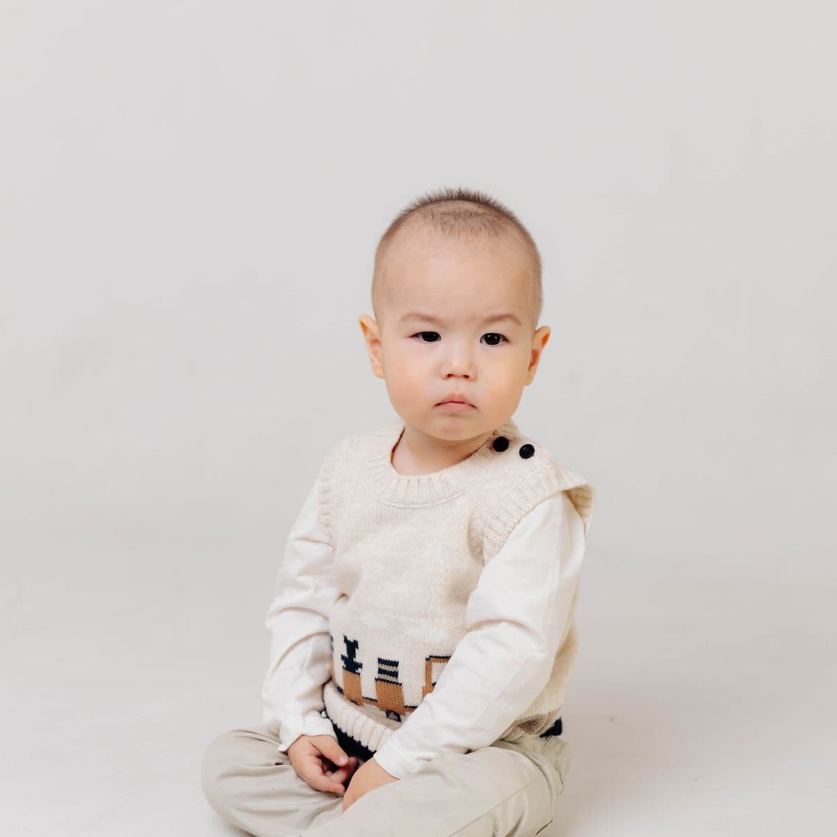 Baby in a cream knit vest over an ivory tee