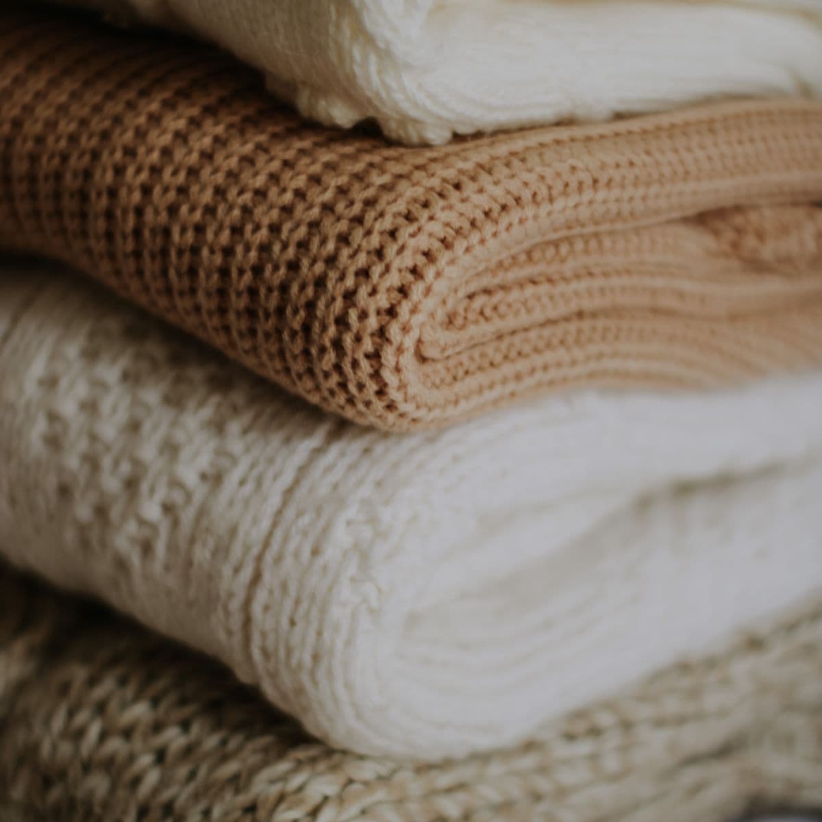 A small stack of folded knit basics in tan and cream