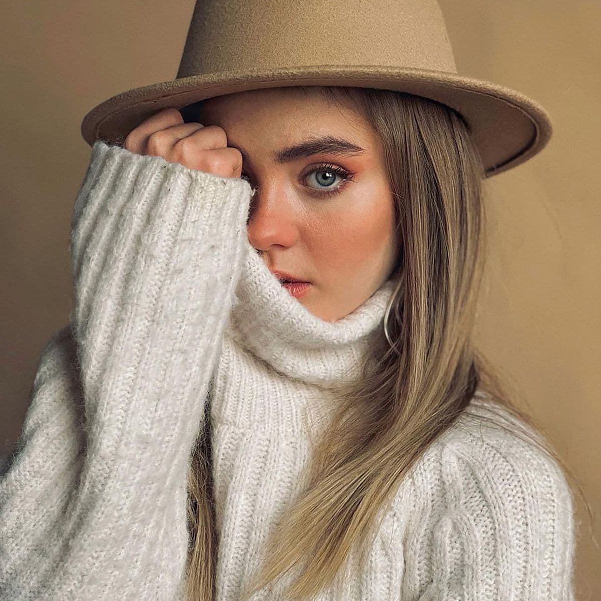 Woman in a cream cable-knit turtleneck and felt hat