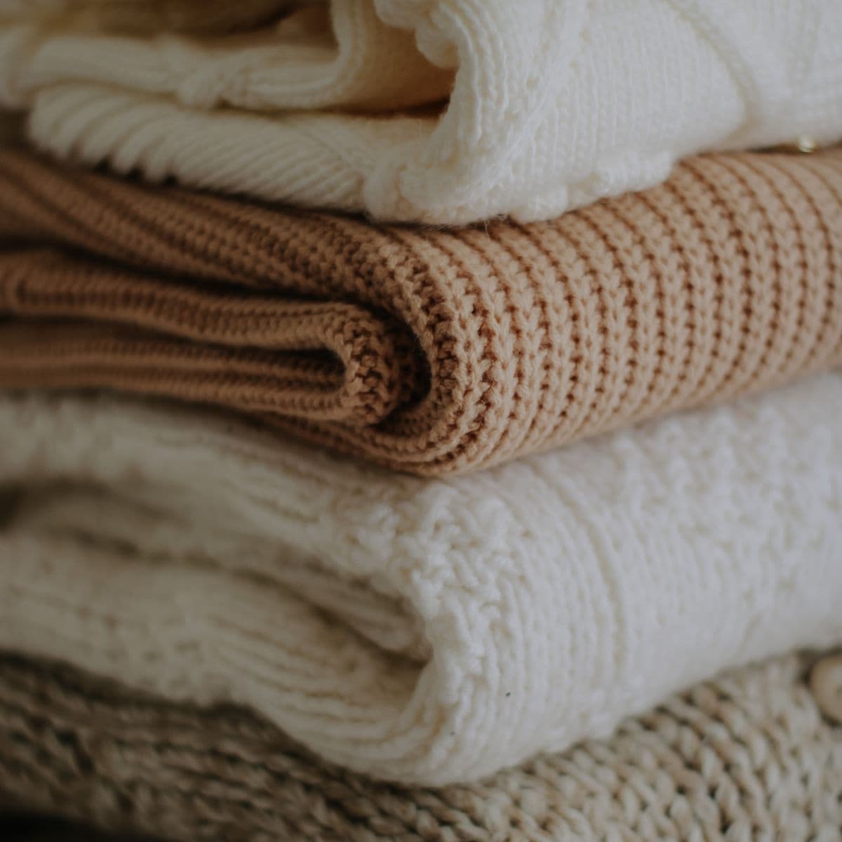 A folded stack of cream and camel sweaters
