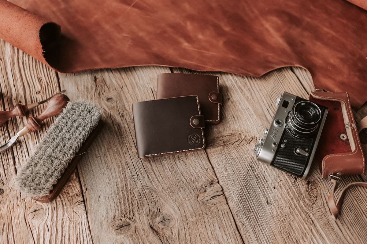 A brown leather wallet and accessories on a wood surface