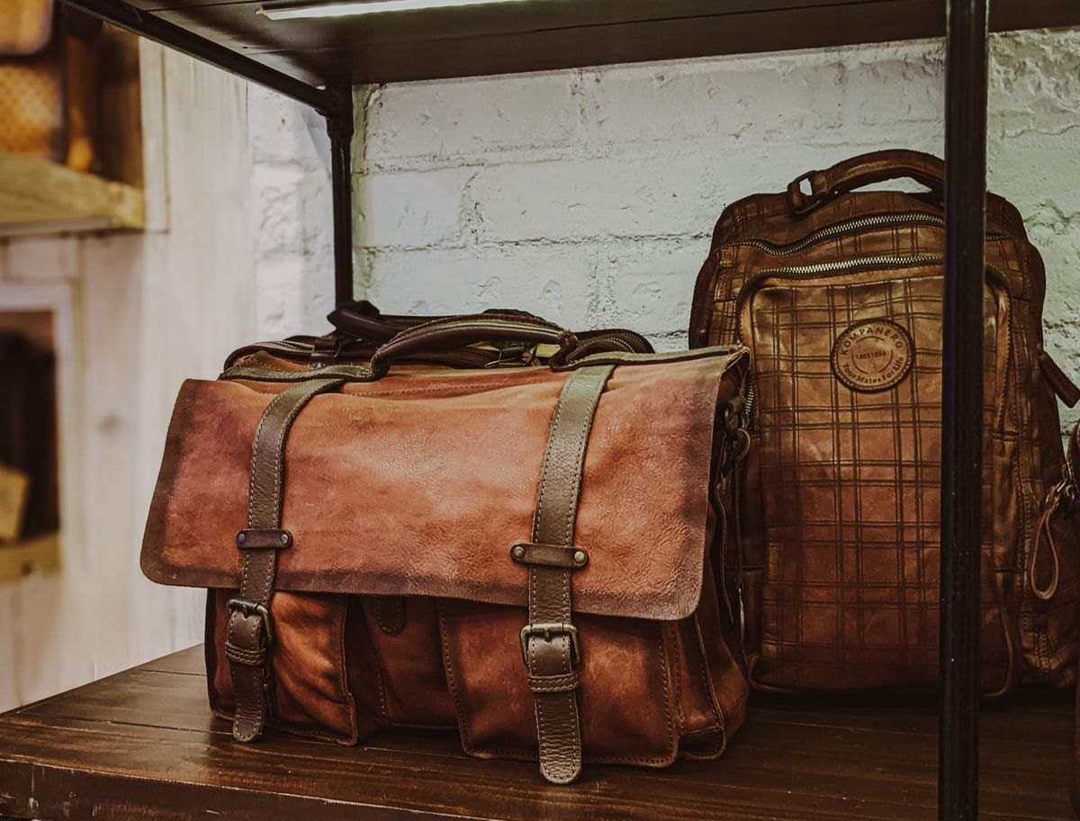 A tan leather messenger bag and backpack on a shelf