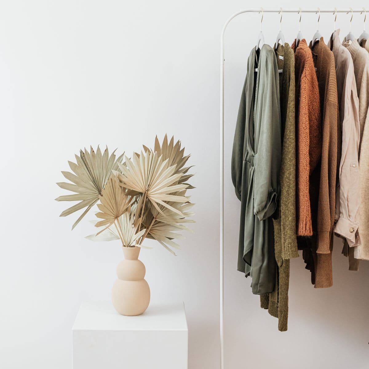 A styled rack of muted dresses beside dried palm