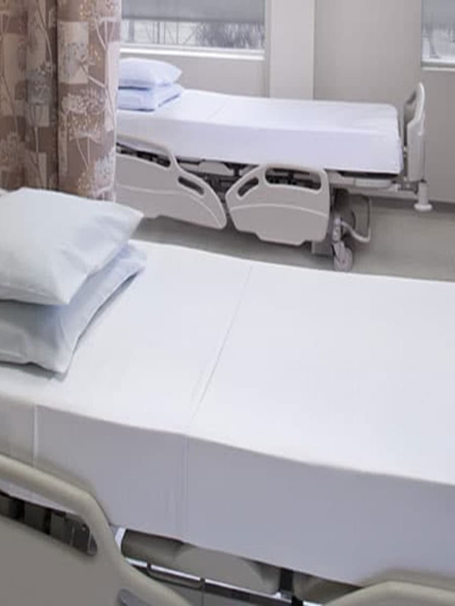 A hospital ward bed made up with taut white linen and a blue pillow