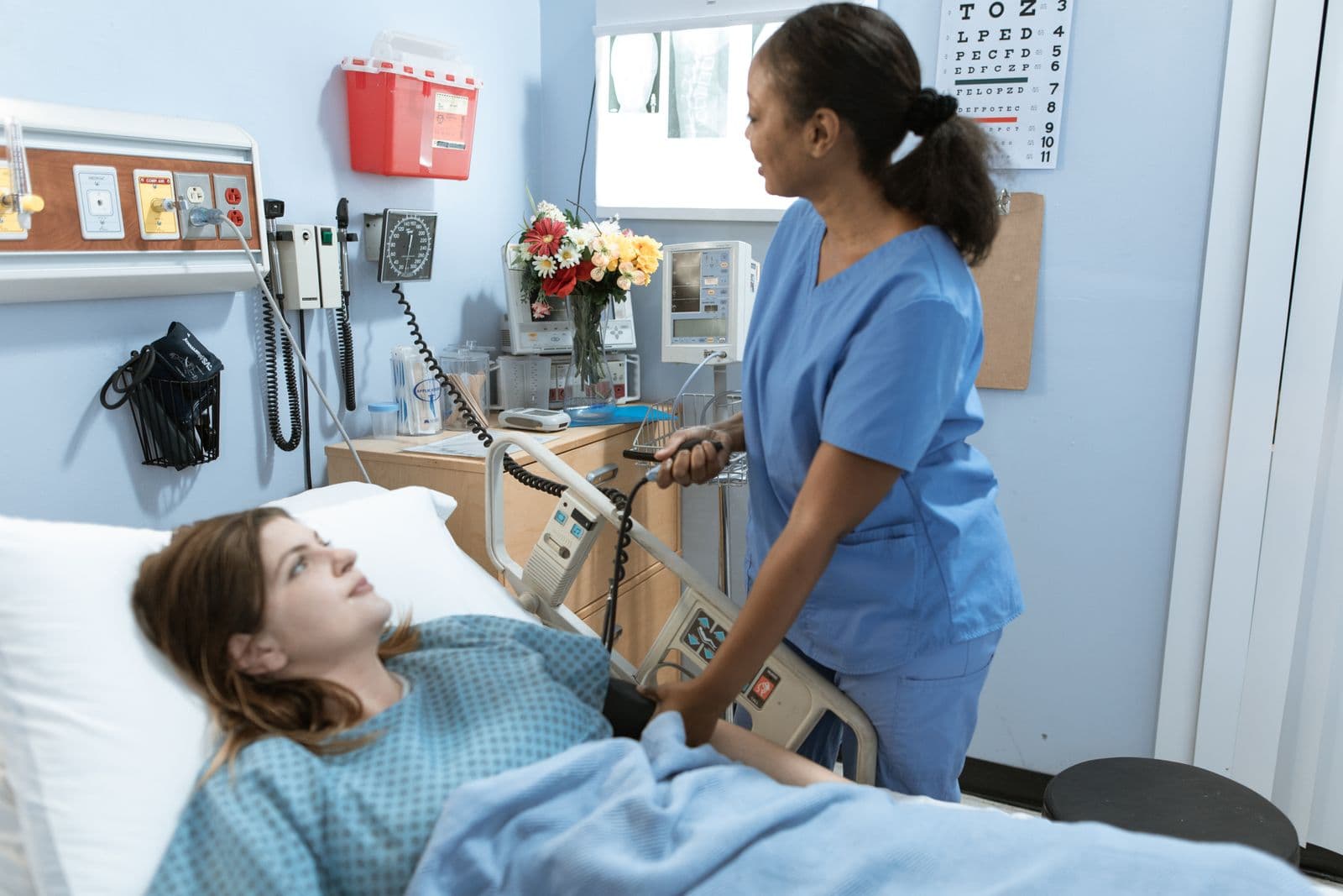 A nurse in scrubs caring for a patient in a gown on a hospital ward