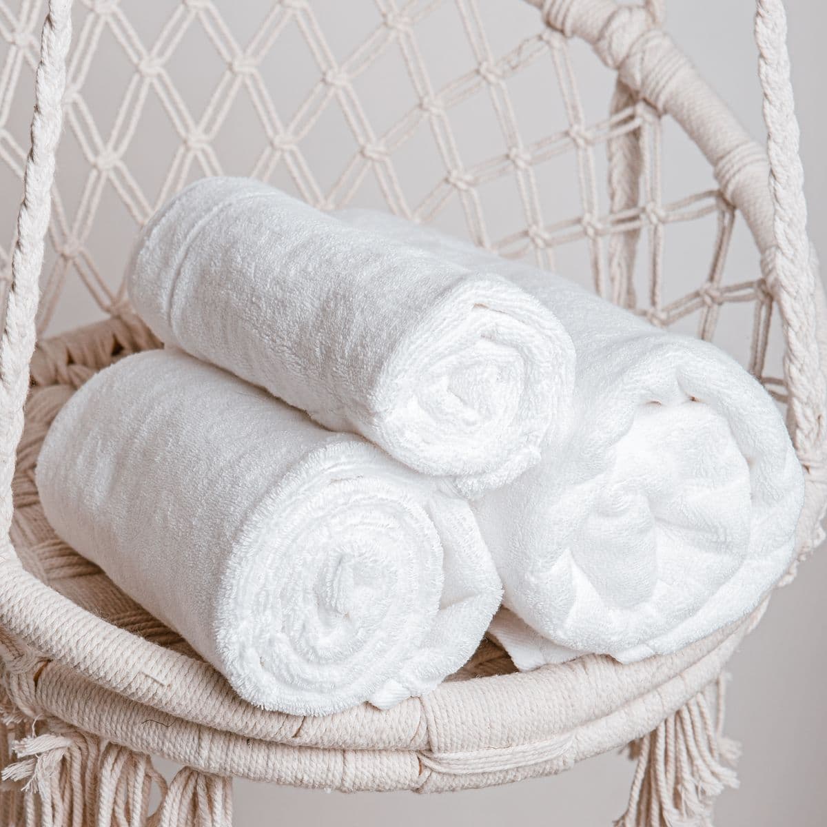 Three rolled white bath towels in a soft ivory chair