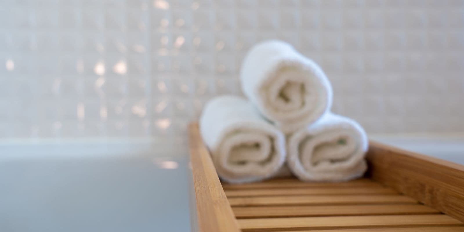 White rolled towels on a bamboo tray in a bright airy bathroom