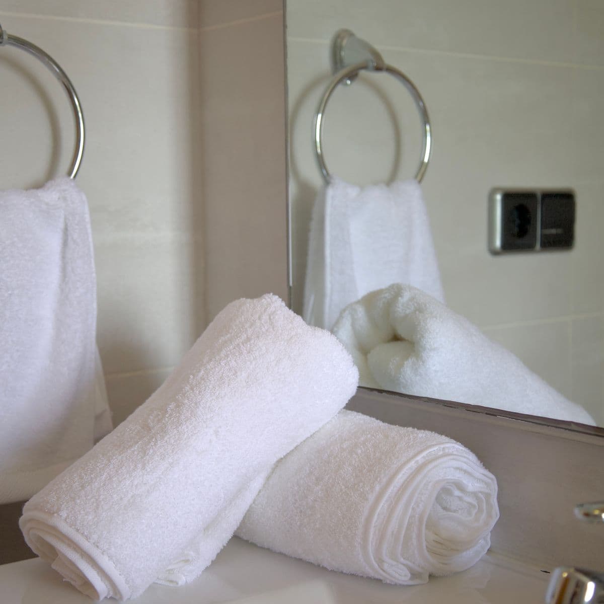 Rolled and ring-hung white hotel towels by a mirror