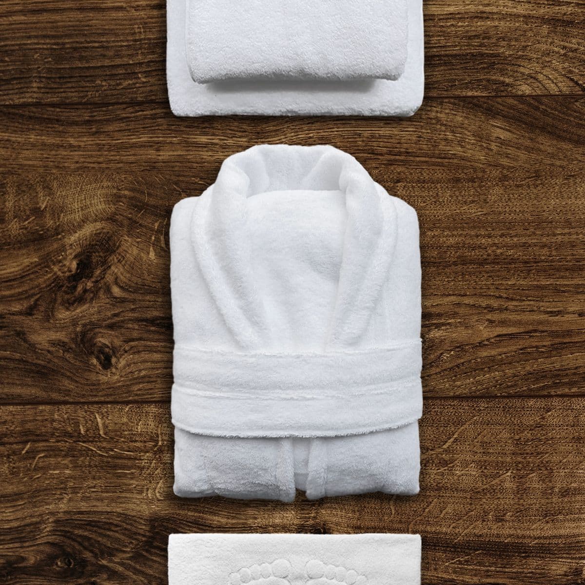 A neatly folded white towelling bathrobe with matching bath towels