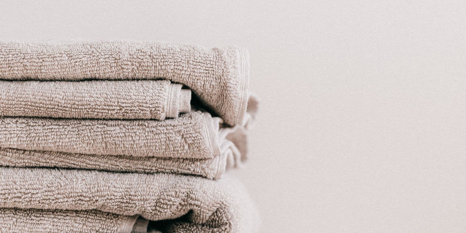 A soft stack of folded stone-ivory bath towels against a bright wall