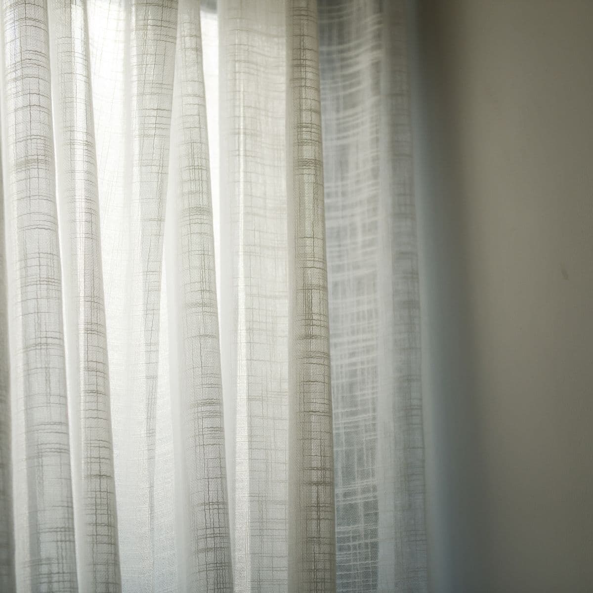 A light ivory linen-weave sheer curtain panel softly lit