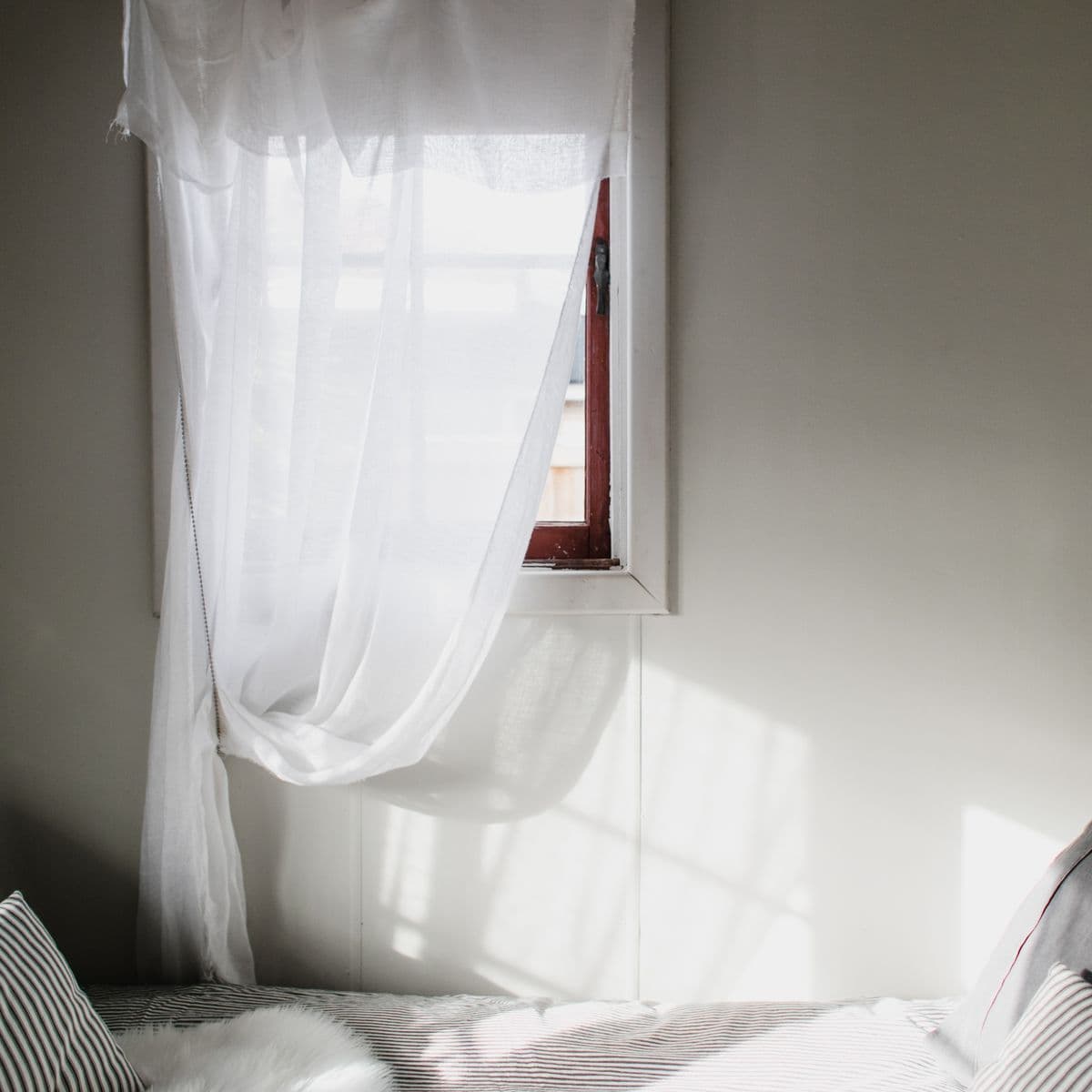 A floor-length white sheer curtain at a sunlit window