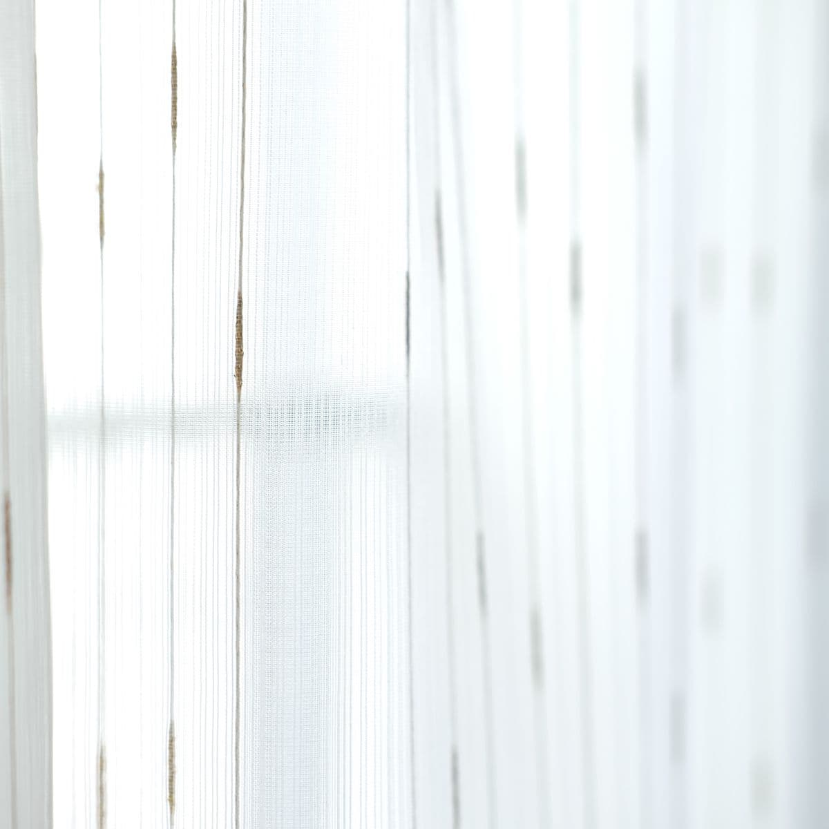 A crisp white sheer curtain with a delicate dotted weave
