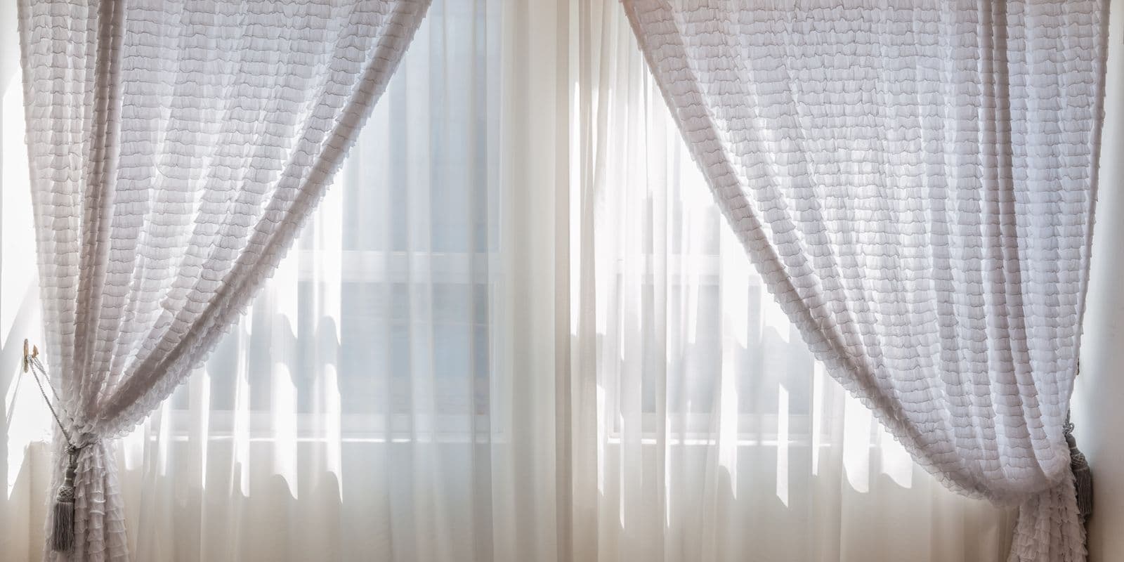 Elegant white sheers tied back at a bright sunlit window