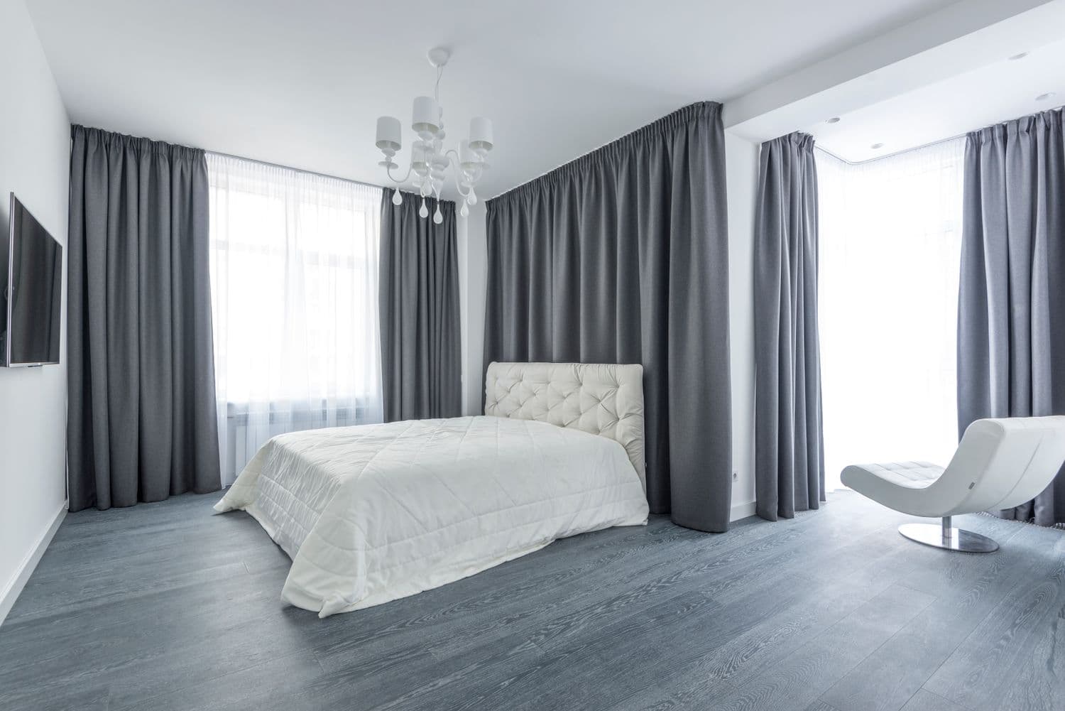 Soft grey lined drapery beside a crisp white bed