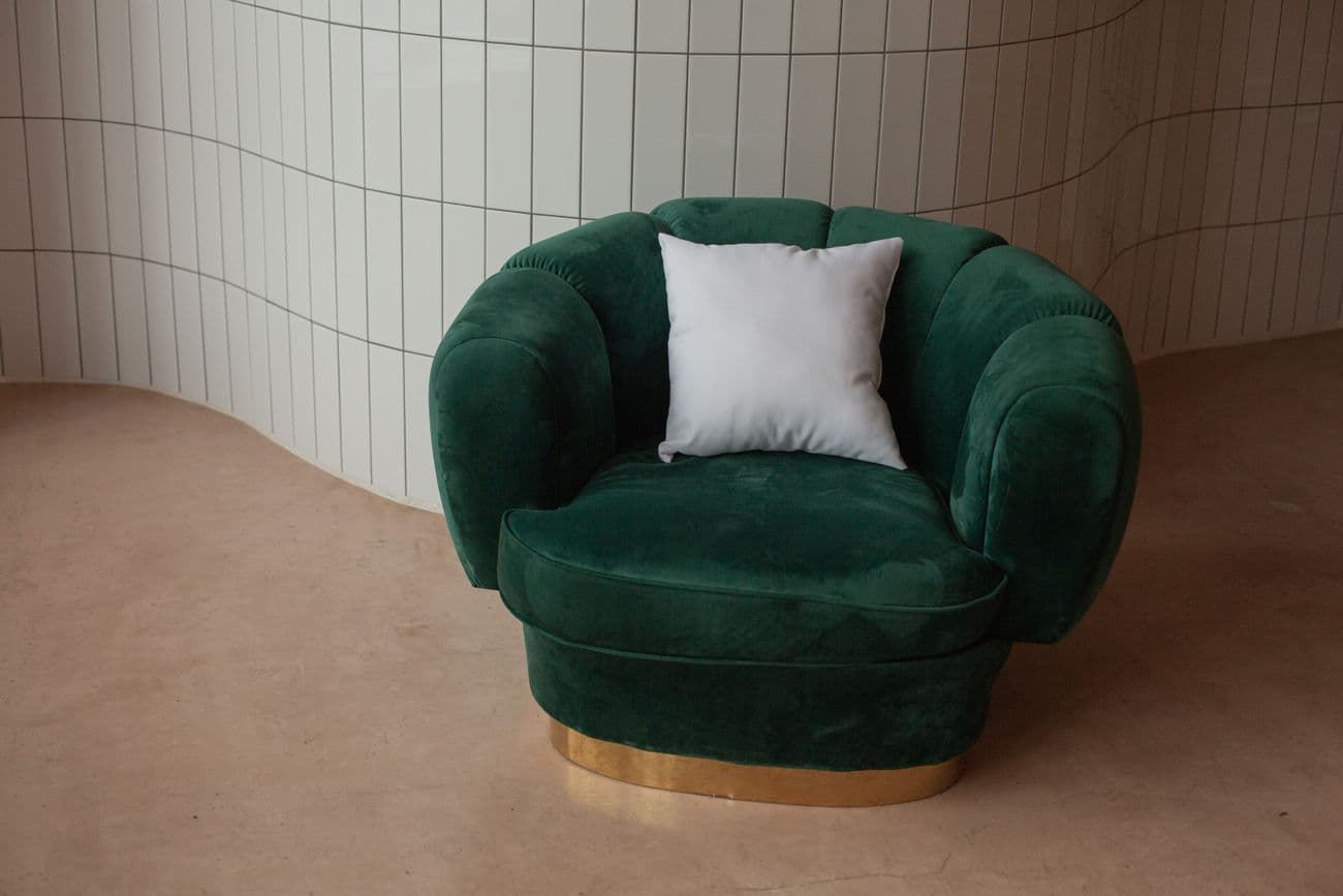 A white scatter pillow on an emerald green velvet chair