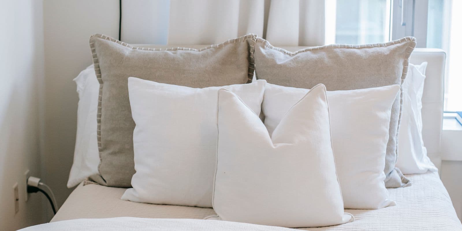 White and stone linen cushions layered on a bright airy bed