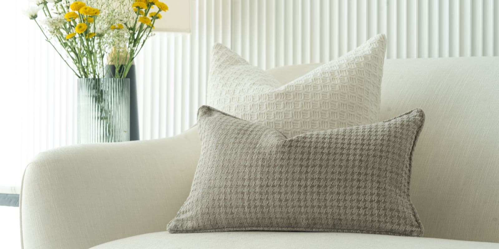 Cream and grey woven cushions arranged on an ivory bouclé sofa