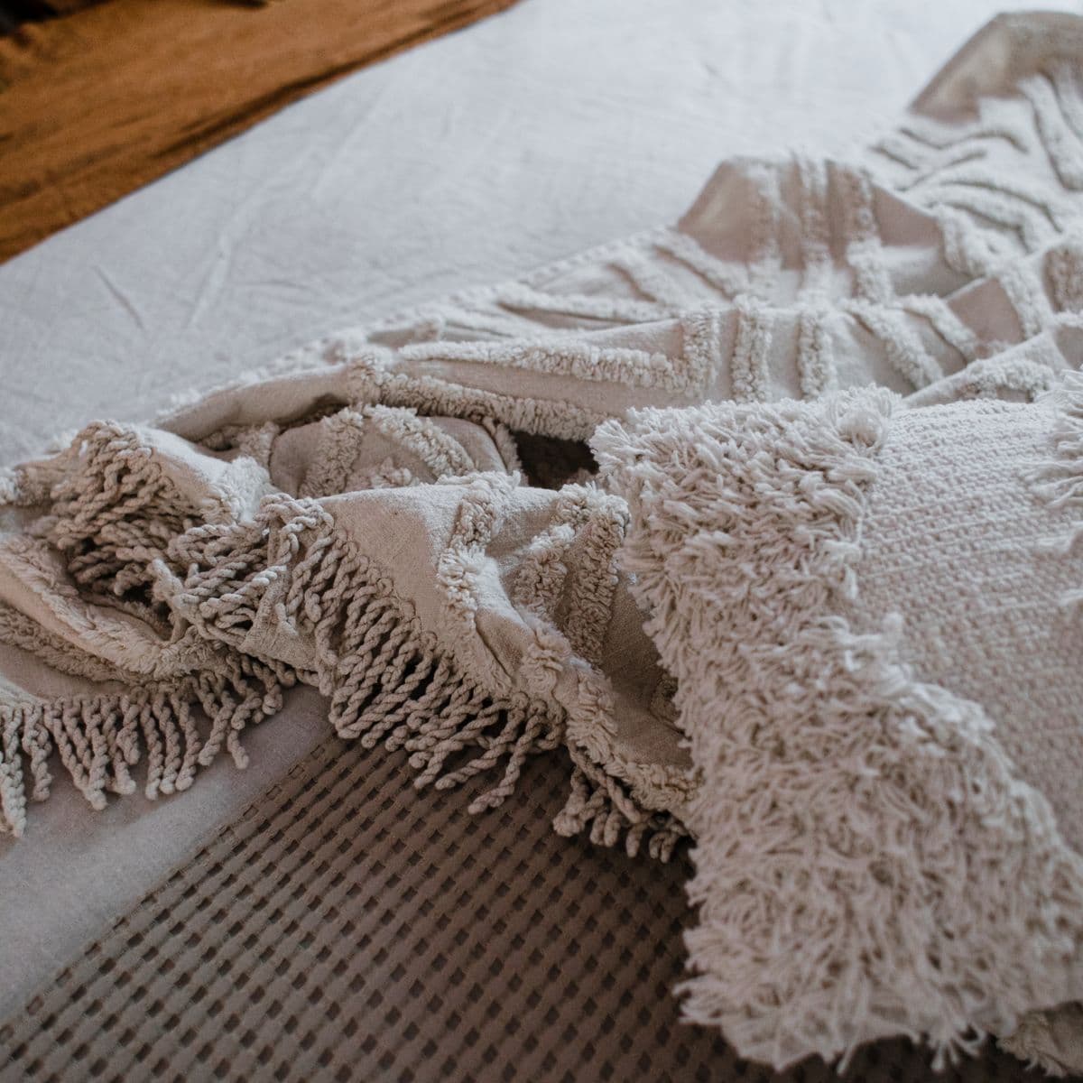A cream tufted and fringed throw folded over neutral linen