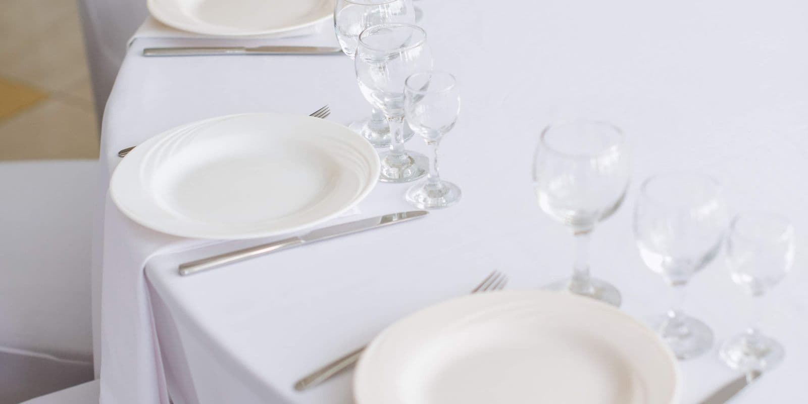 A crisp white banquet table laid with white plates and crystal glasses