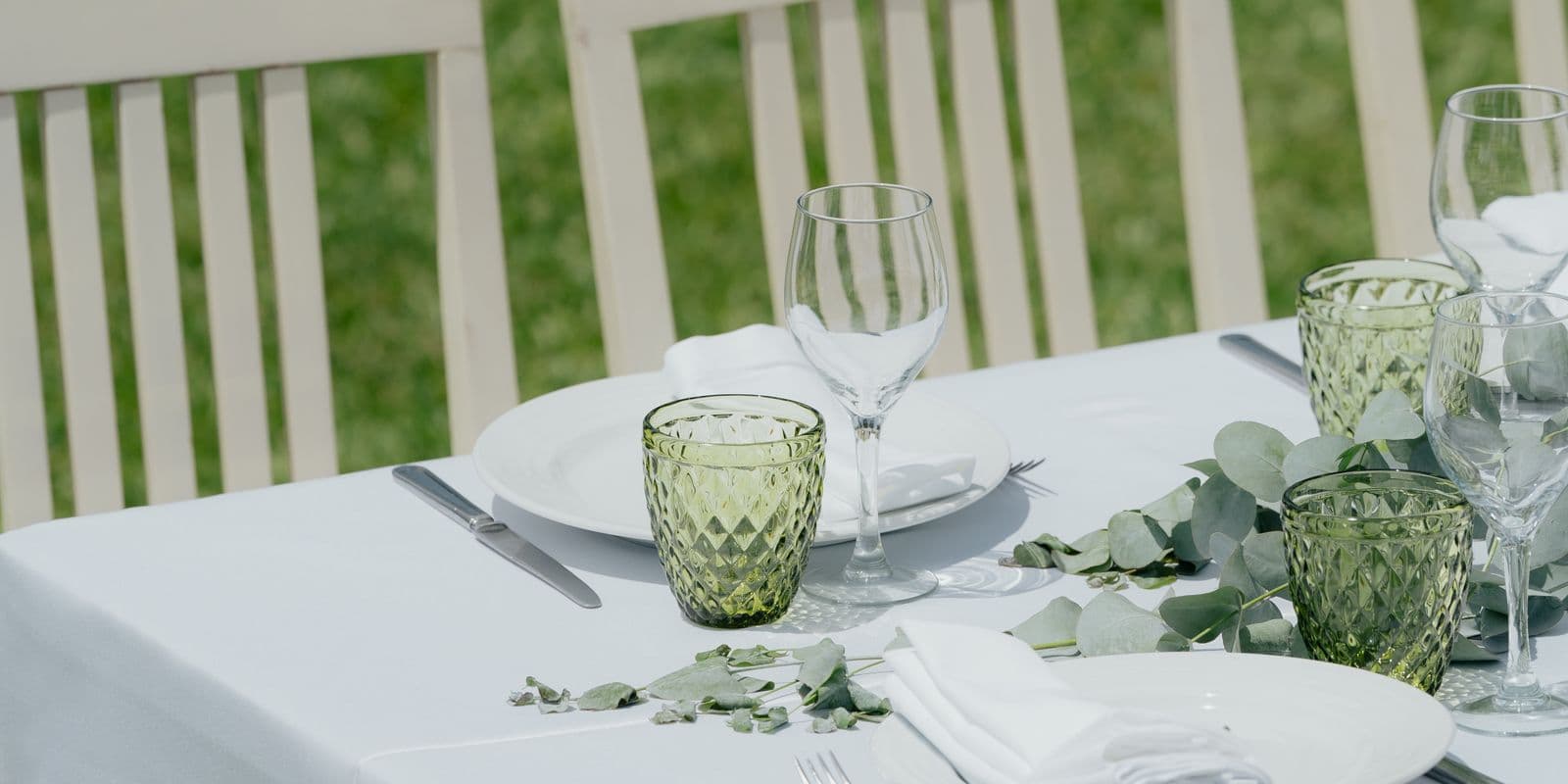 A long white-linen table dressed with glassware and greenery