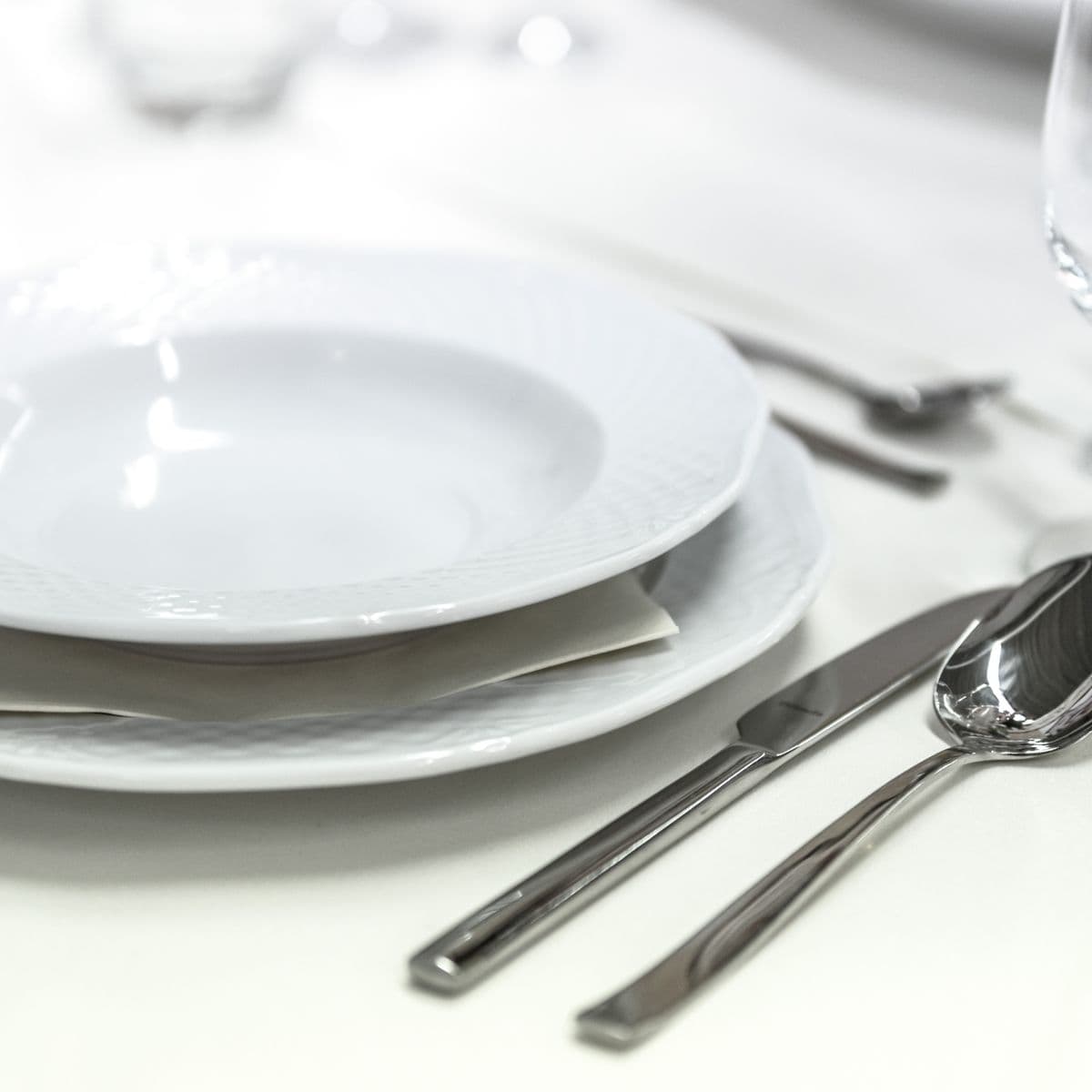Stacked white porcelain plates and polished silverware on white linen