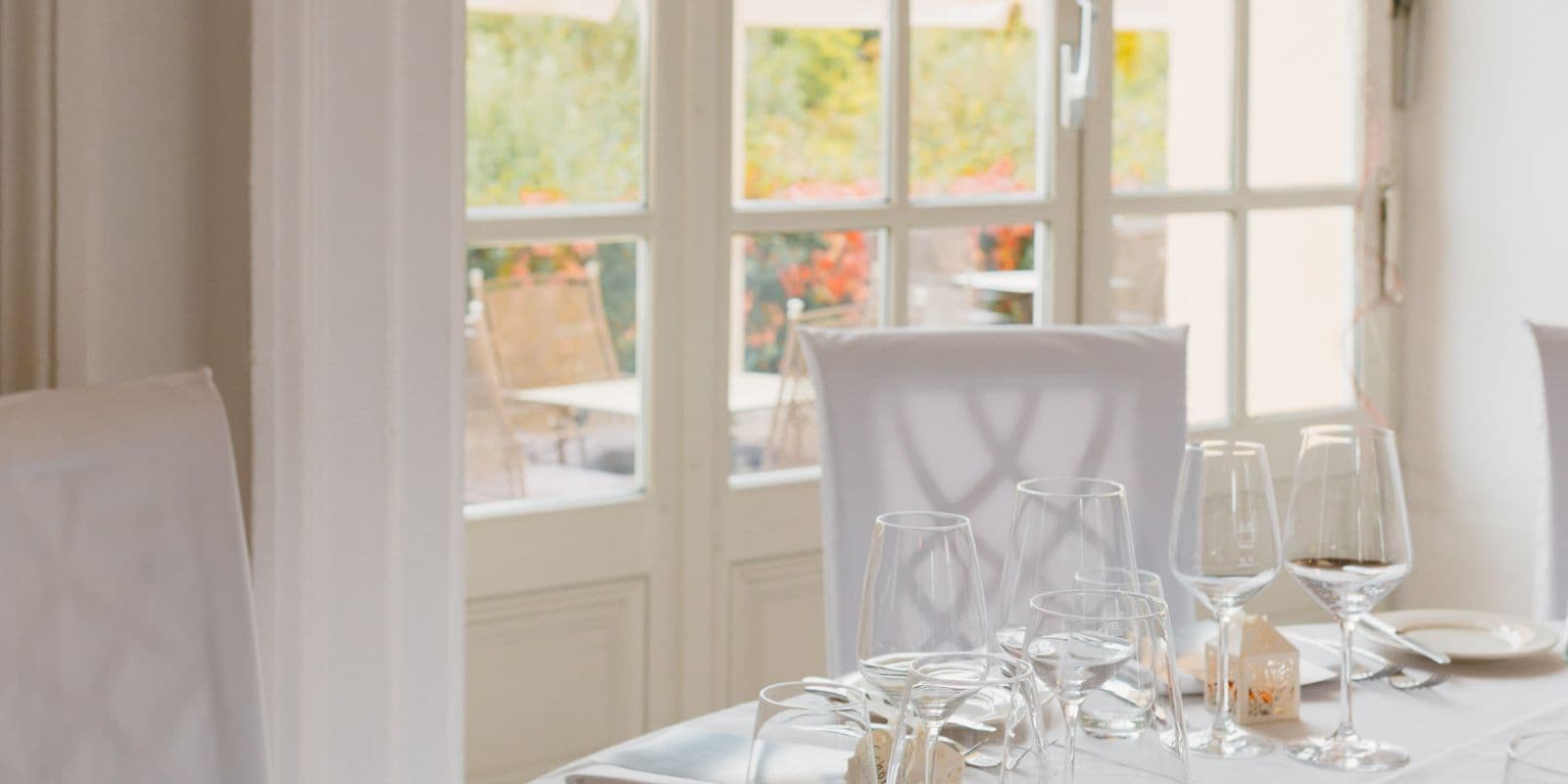 A bright dining room with white-draped chairs and crisp white table linen