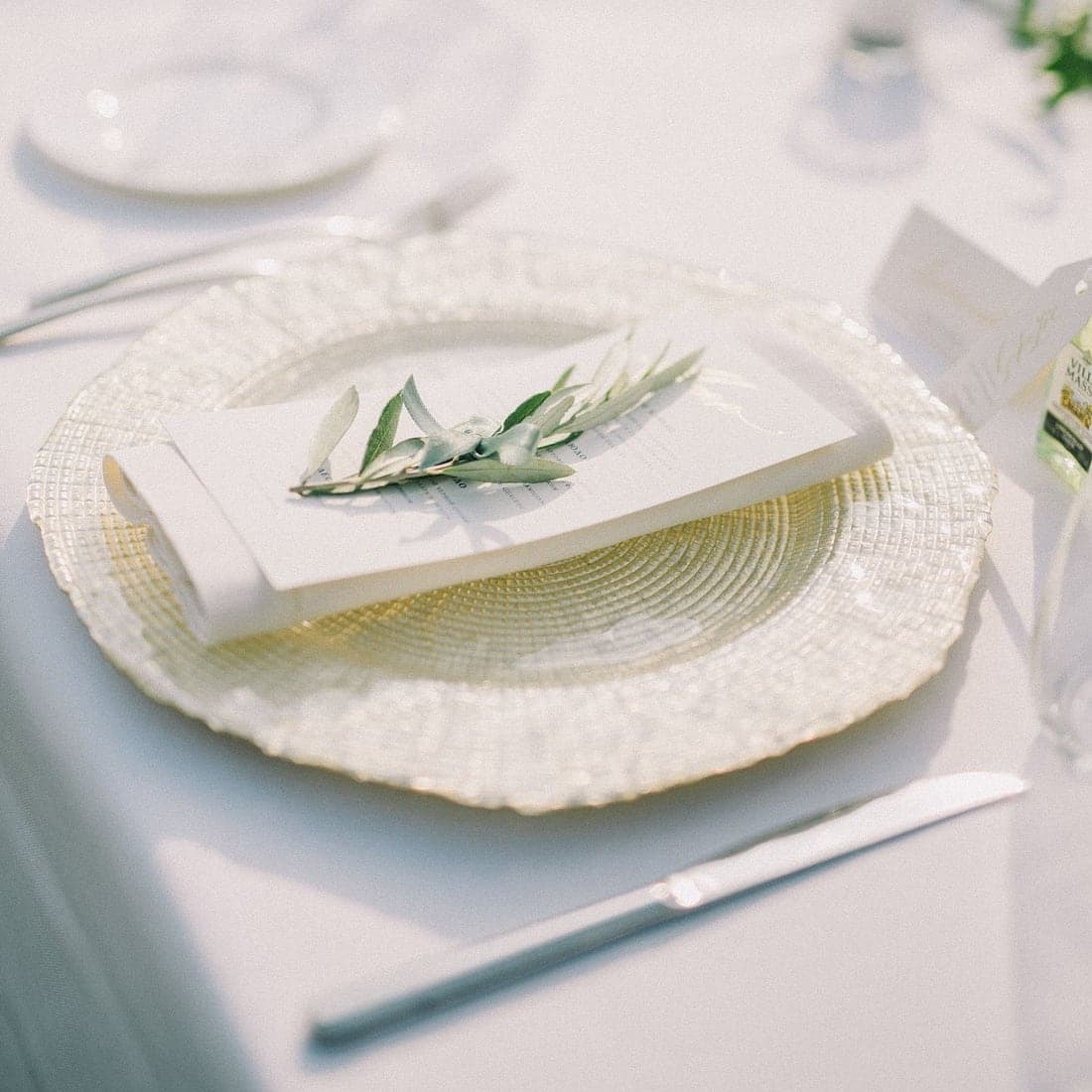 An elegant all-white place setting with a menu card and olive sprig