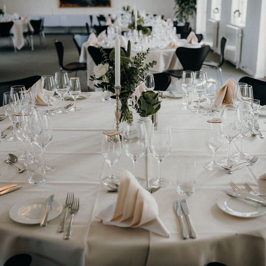 A round banquet table dressed in ivory linen with fan-folded napkins