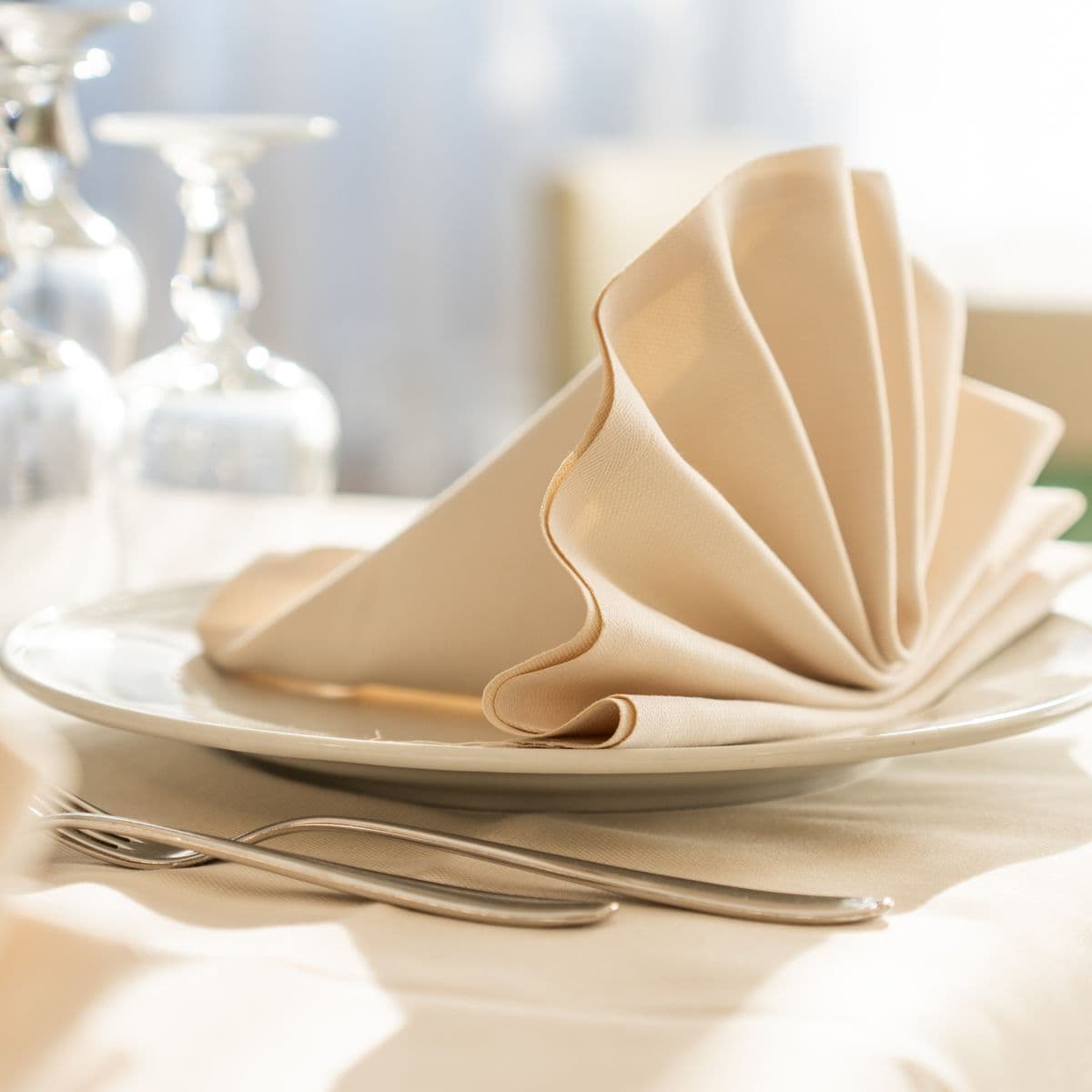 A crisp linen dinner napkin fan-folded on a white plate with silverware