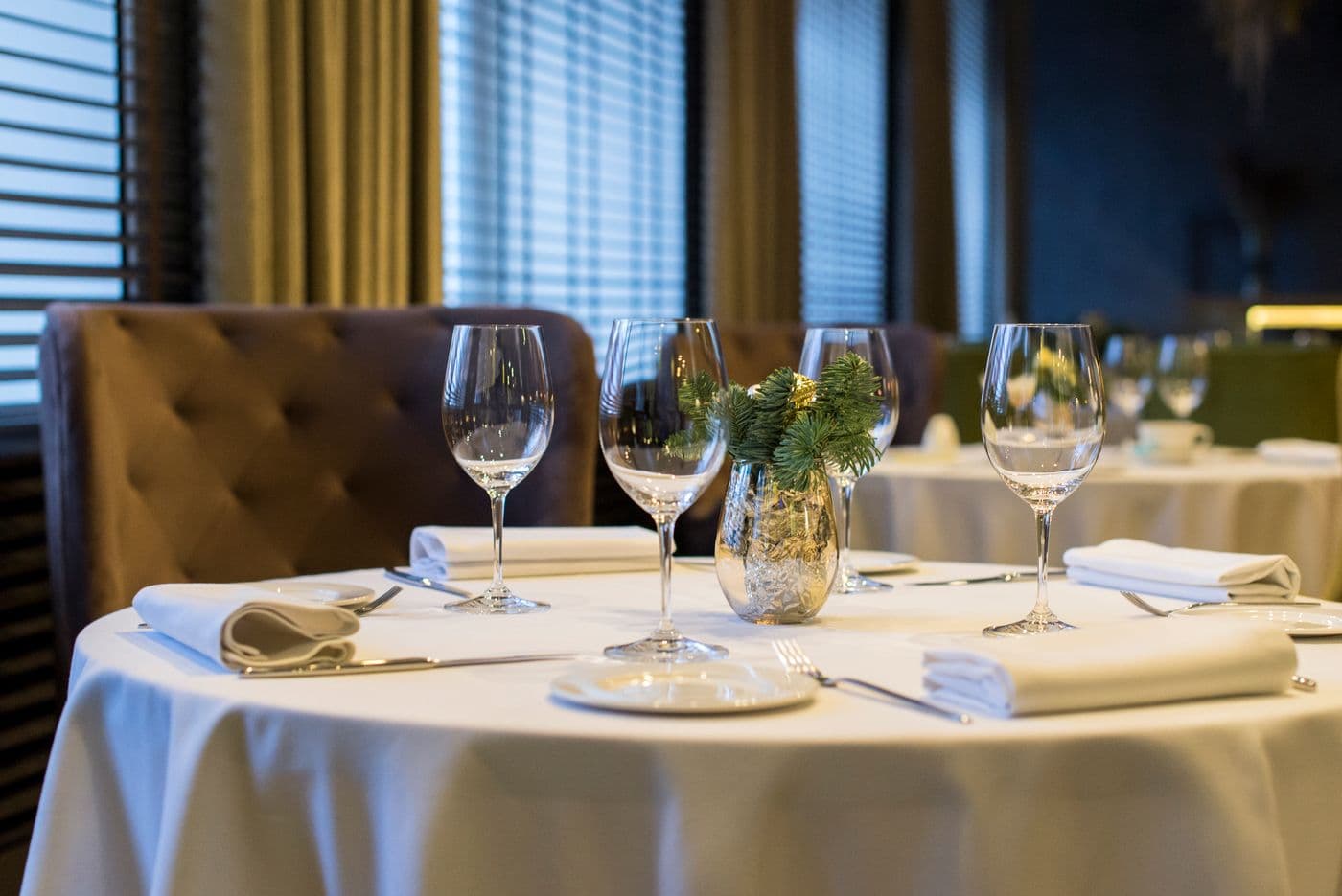 A round table dressed in white linen with glassware