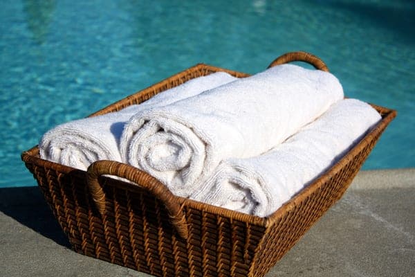 Rolled towels in a woven basket beside a pool