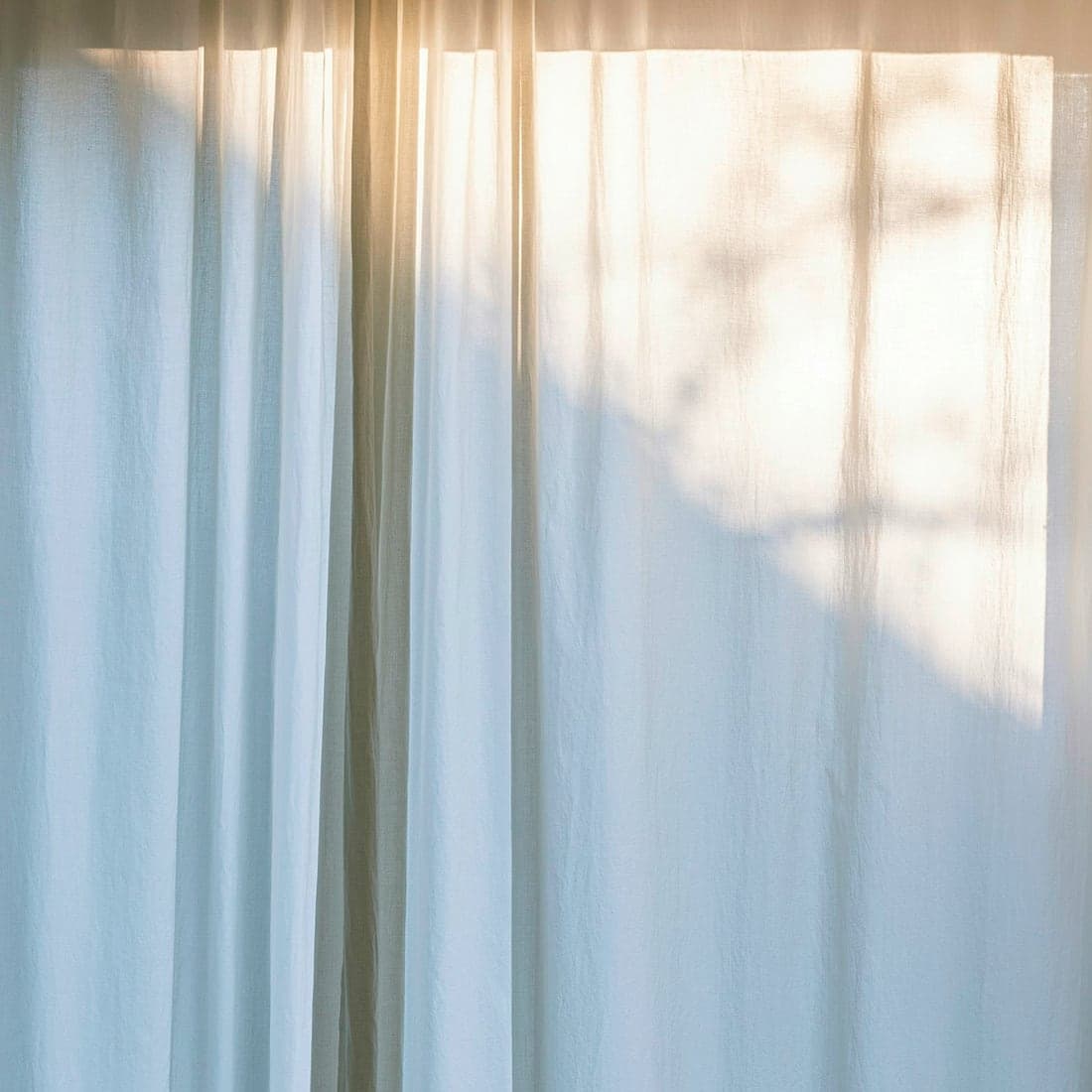 A sunlit white sheer curtain panel