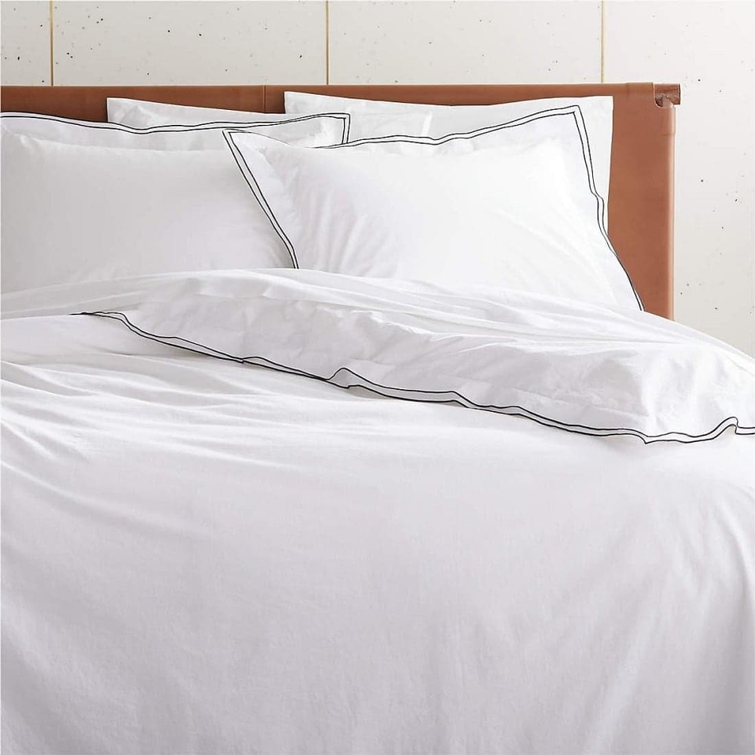 A bed dressed in crisp white linen with a tan headboard