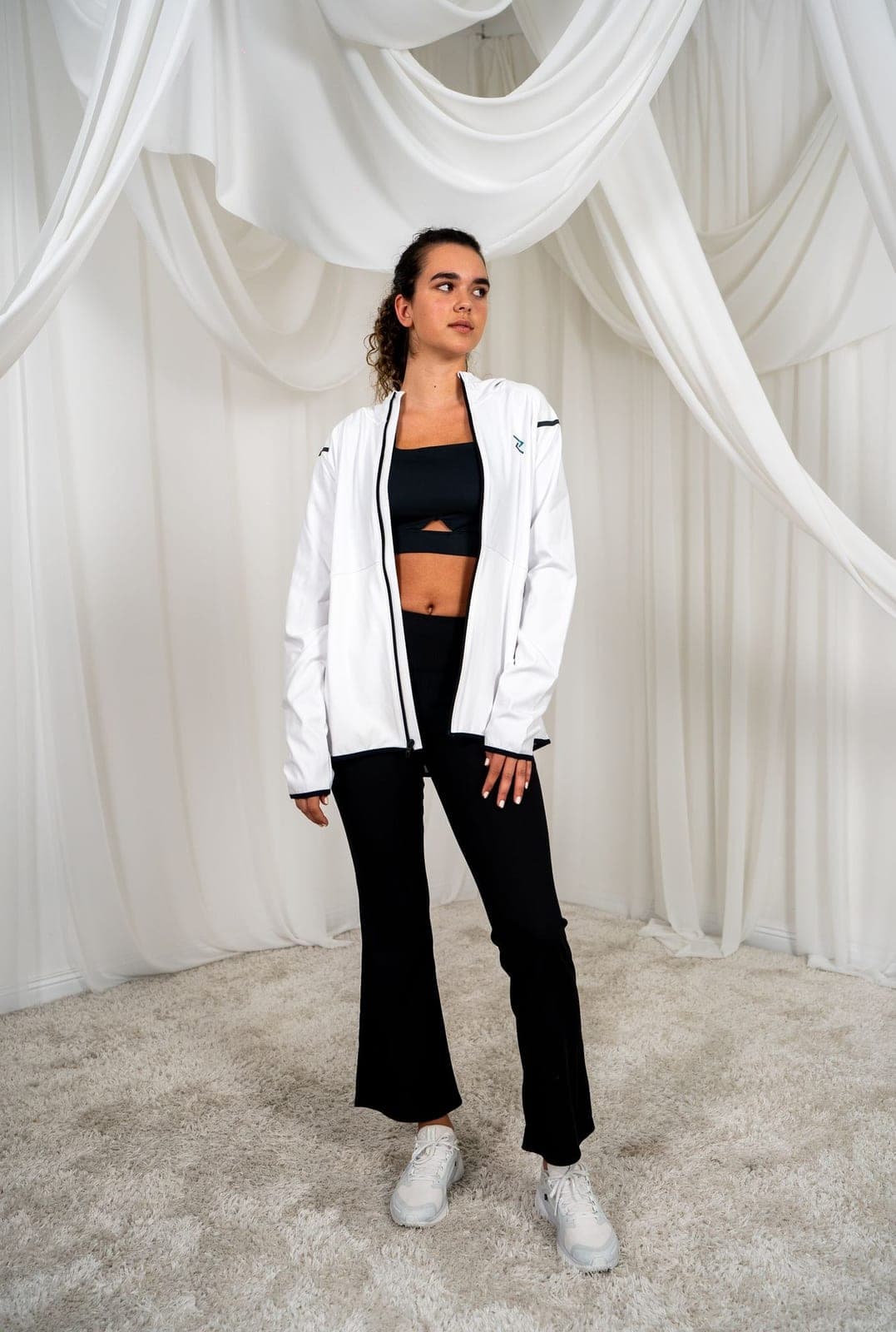 A woman in a white activewear jacket and leggings against a light backdrop