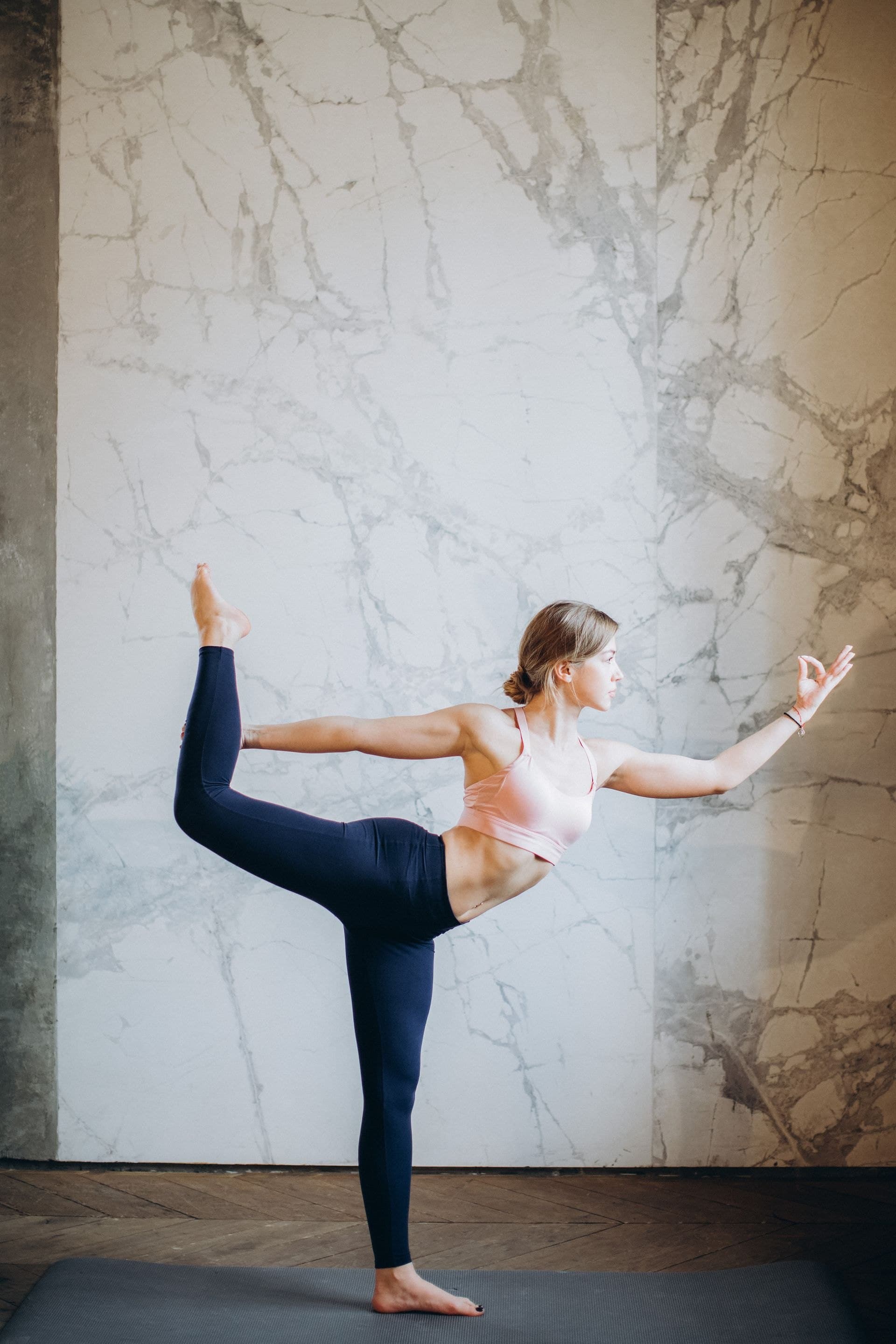 A model in a pink sports bra and navy leggings in a yoga pose against marble