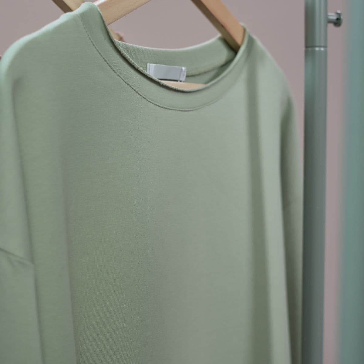 A sage athletic sweatshirt on a wooden hanger