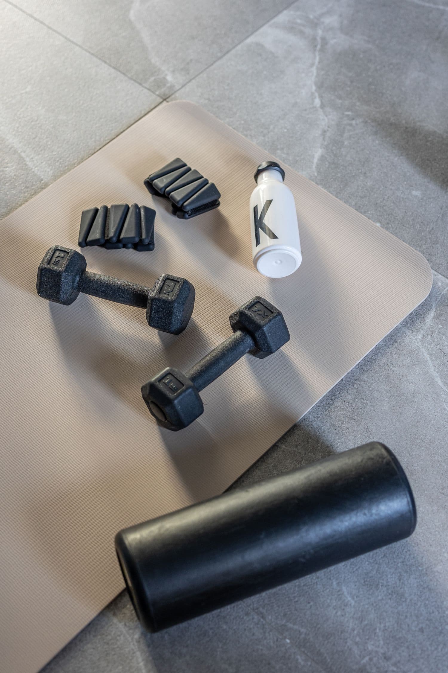 A soft, light flat lay of dumbbells, a bottle and a foam roller