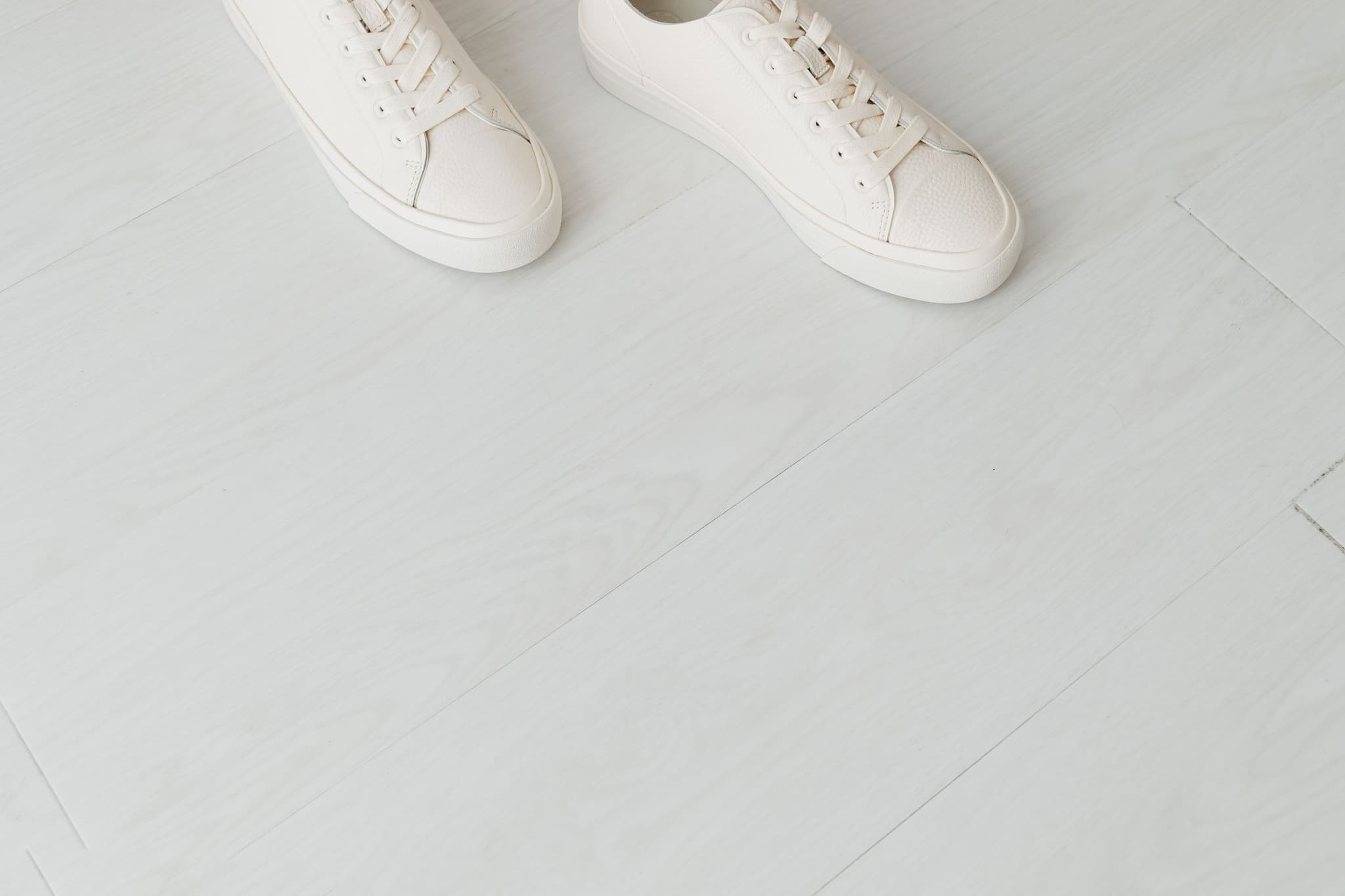 A pair of clean white trainers on a soft, light wooden floor