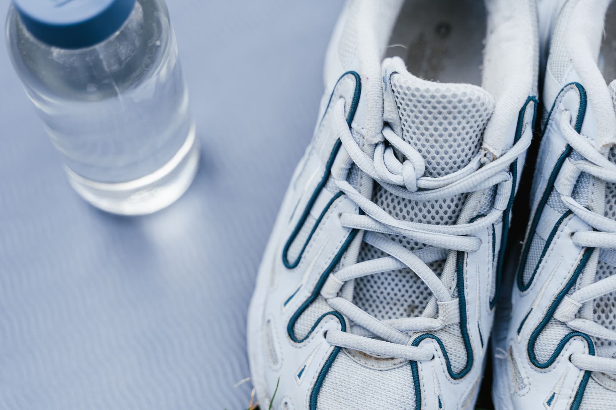 White running shoes beside a sports water bottle in soft, bright light