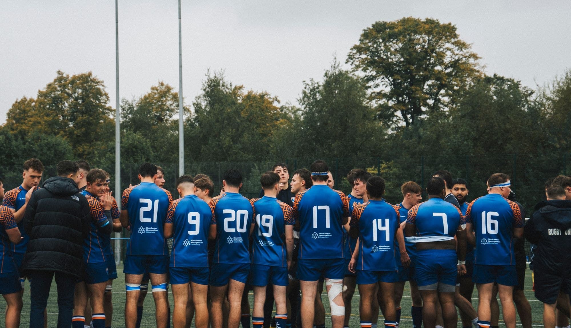 A rugby team huddled in matching sublimated, numbered club kit
