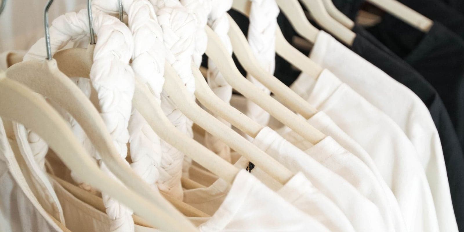A row of crisp white shirts on wooden hangers