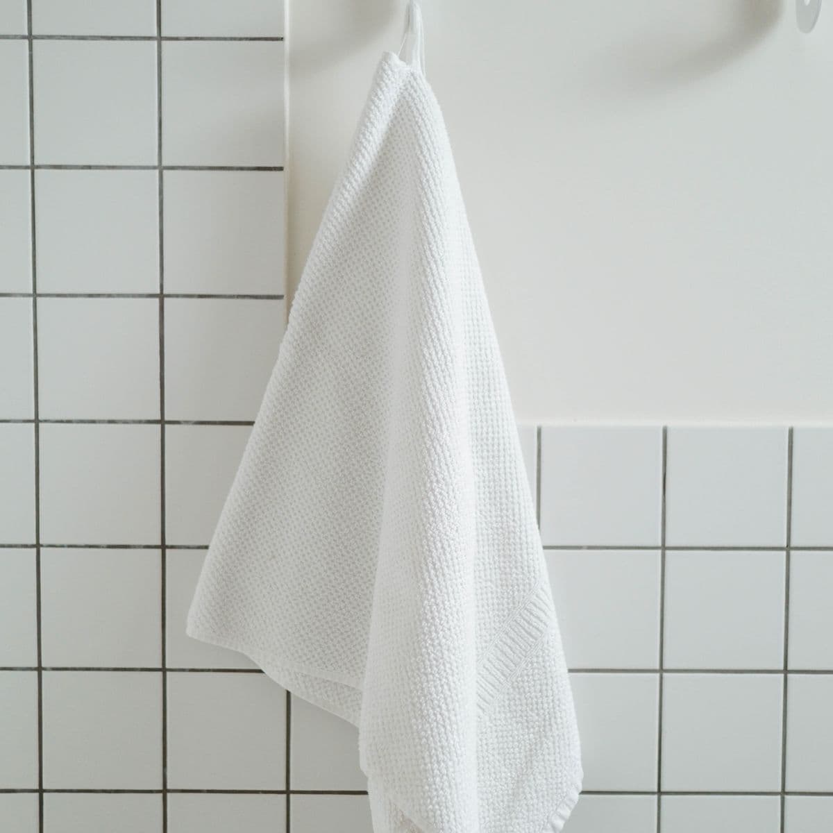 A white waffle-weave hand towel against bright white tiles